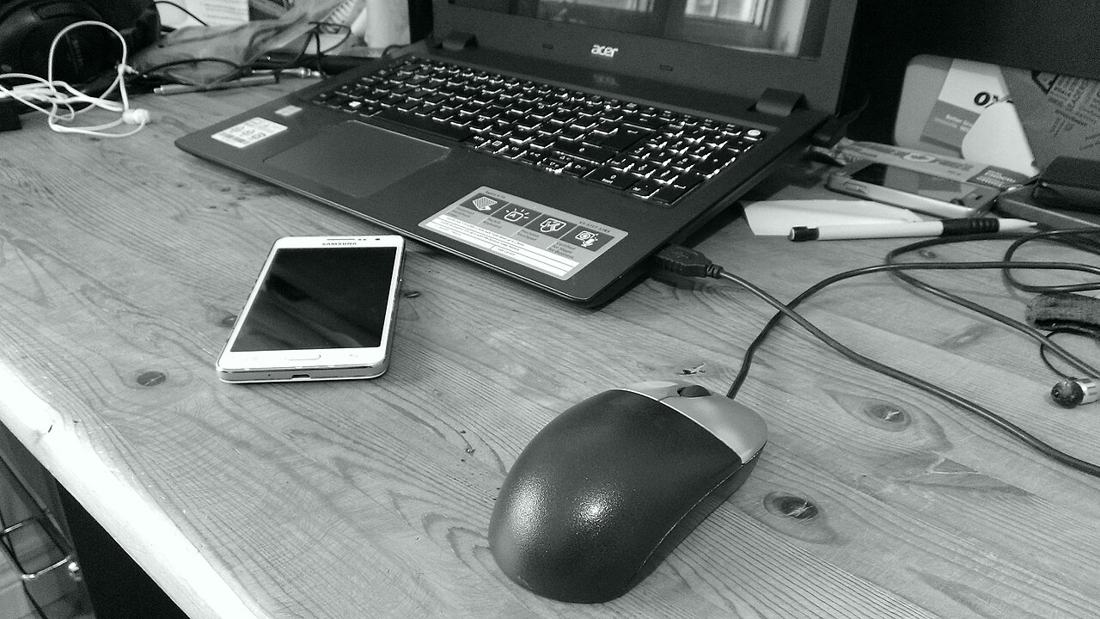 A computer mouse, laptop and phone on a desk.