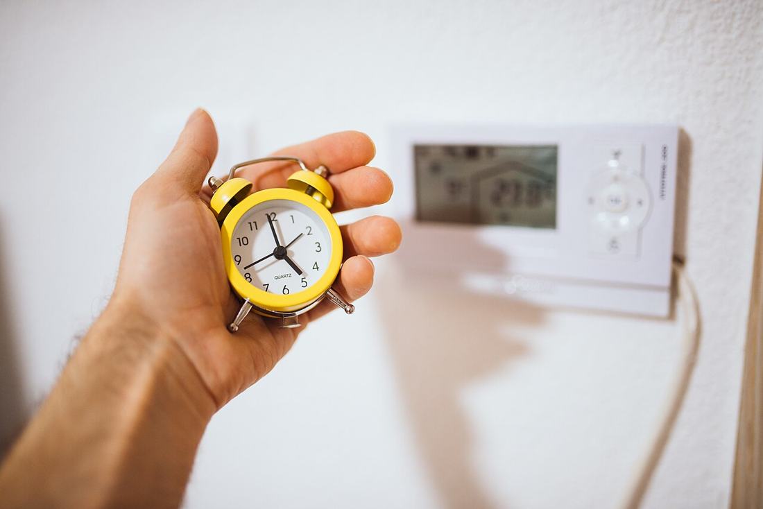 A hand holding a vintage yellow alarm clock indoors.